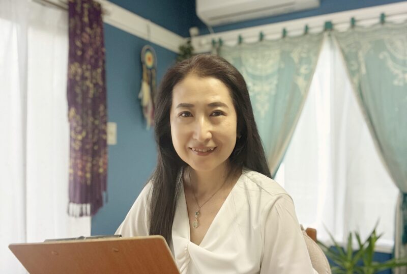 サロンのテーブルに座り、微笑んでいるラナヒ。カウンセリングのイメージ。